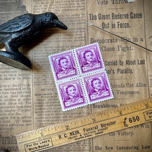 May include: Four purple United States postage stamps featuring a portrait of Edgar Allan Poe. Each stamp has a value of 3 cents. The stamps are arranged in a 2x2 grid and are placed on a newspaper background.