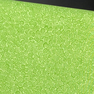 May include: Bright green fabric with a repeating swirl pattern. The fabric is a light green color with a darker green swirl design. The fabric is rolled up, showing the pattern and texture. This fabric is suitable for quilting, sewing, and crafting projects.