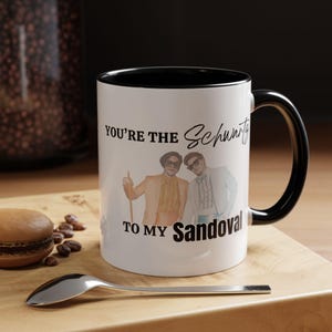 May include: White ceramic mug with a black interior and handle. The mug features an image of two men in suits and sunglasses, with the text "You're the Schwartz to my Sandoval."