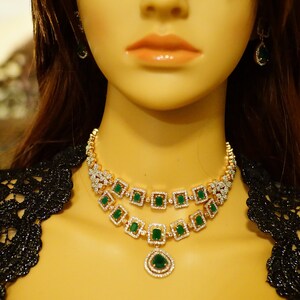 May include: A gold necklace with a double row of emerald green and clear stones. The necklace has a teardrop pendant with a similar design.