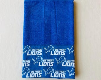 May include: A blue towel with a white border featuring a repeated pattern of a lion and the words "Detroit Lions".