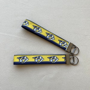 May include: Two yellow and navy blue keychains with a repeated pattern of a hockey team logo. The keychains have silver key rings.