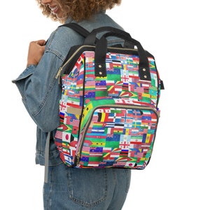 May include: A black backpack with a large zippered pocket and a smaller pocket on the front. The backpack is covered in a colorful pattern of flags from around the world.