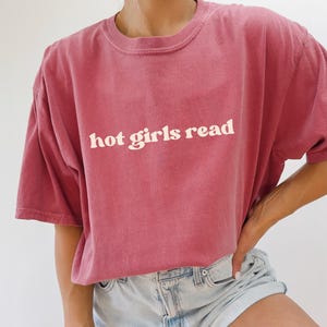 Puede incluir: Una camiseta de color carmes&iacute; con el texto "hot girls read" en blanco.