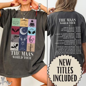 Może przedstawiać: Ciemnoszary t-shirt z krótkim rękawem, z przodu ozdobiony siatką ilustracji fantasy oraz napisem "THE MAAS WORLD TOUR". Z tyłu znajduje się lista tytułów książek i dat pod tym samym nagłówkiem "THE MAAS WORLD TOUR".