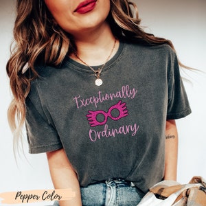 May include: A gray t-shirt with a pink graphic that says "Exceptionally Ordinary" with a pair of pink glasses with wings.