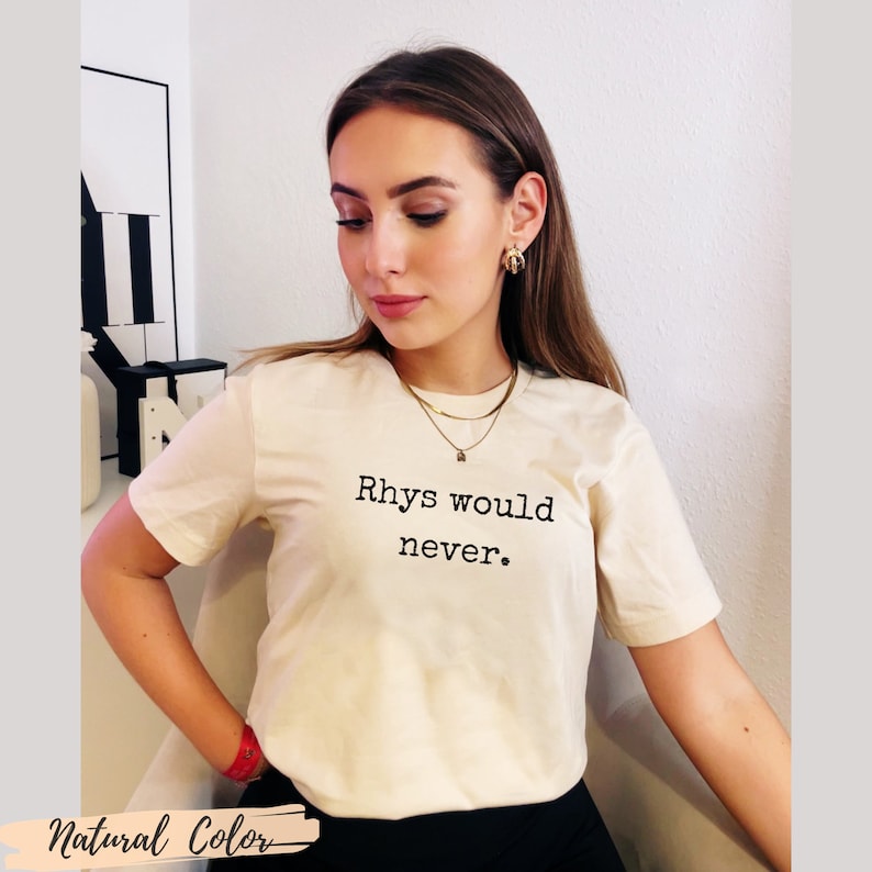 Puede incluir: Una camiseta blanca con el texto "Rhys would never." impreso en negro.