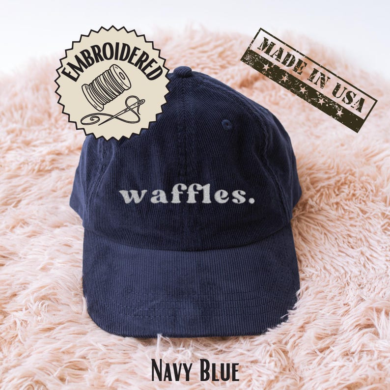 Peut inclure: Casquette de baseball en velours c&ocirc;tel&eacute; bleu marine avec le mot "waffles" brod&eacute; en blanc. La casquette a une visi&egrave;re incurv&eacute;e et un bouton sup&eacute;rieur. L'image comprend &eacute;galement un tampon "Made in USA" et un motif brod&eacute;.