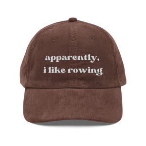 May include: A brown corduroy baseball cap with the embroidered text "apparently, i like rowing" in white. The cap has a curved brim and a small button on top. This hat is a casual accessory.