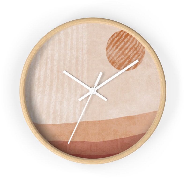 May include: A round wall clock with a wooden frame and a beige background. The clock face features a minimalist design with a sun-like shape in the top right corner and a horizontal line pattern in the bottom half. The clock hands are white.