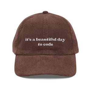 Può includere: Cappellino da baseball in velluto a coste marrone con la scritta ricamata in bianco "it's a beautiful day to code". Il cappellino ha una visiera curva e un bottone sulla parte superiore.