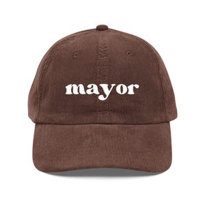 以下が含まれることがあります： 前面に白い文字で「mayor」と刺繍された茶色のコーデュロイ野球帽。カーブしたつばと丸みを帯びたトップが特徴です。