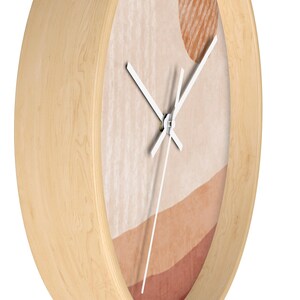 May include: A wooden wall clock with a white face and white hands. The clock face has an abstract design with shades of brown, beige, and peach.