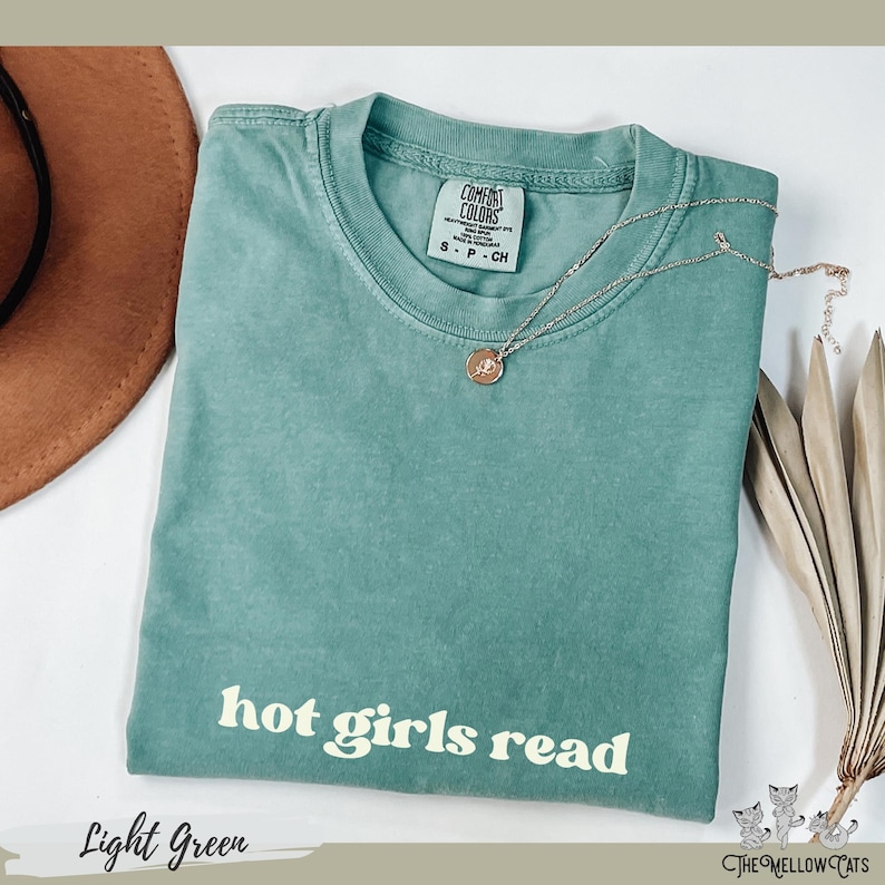 Puede incluir: Camiseta verde claro con el texto "hot girls read" en una fuente retro.