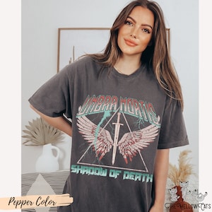 May include: A dark gray t-shirt with a vintage graphic print of a winged sword in a triangle with the text "Umbra Mortis Shadow of Death".