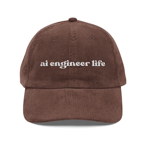 May include: A brown corduroy baseball cap with the text "ai engineer life" embroidered in white. The cap has a curved brim and a rounded top. This hat is a stylish accessory for anyone in the field of artificial intelligence.