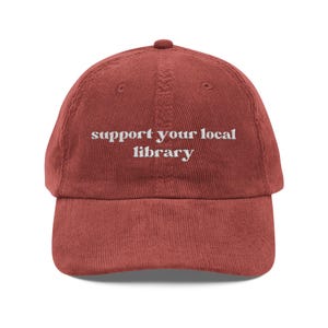 Peut inclure: Casquette de baseball en velours côtelé rouge brique avec l'inscription blanche "support your local library". La casquette a une visière incurvée et une sangle réglable. Un accessoire de mode pour les amateurs de lecture.