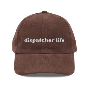Puede incluir: Gorra de béisbol de pana marrón con la inscripción "dispatcher life" bordada en blanco. La gorra tiene una visera curva y una parte superior redondeada.