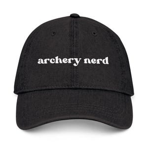 May include: Black baseball cap with the white text "archery nerd" embroidered on the front. The cap has a curved brim and a fabric strap closure on the back. A casual accessory for archery enthusiasts.