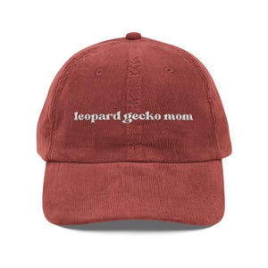 Może przedstawiać: Czapka bejsbolowa z sztruksu w kolorze ceglastym z zakrzywionym daszkiem. Na czapce znajduje się wyszyty białą nicią napis "leopard gecko mom". Czapka ma klasyczny sześciopanelowy design z guzikiem na górze.