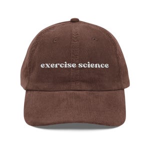 Peut inclure: Casquette de baseball en velours côtelé marron avec l'inscription "exercise science" brodée en blanc. La casquette a une visière incurvée et un dessus arrondi. Un accessoire élégant pour les amateurs de sport et de fitness.