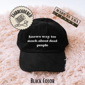 Op de afbeelding: Zwarte corduroy baseballpet met de witte geborduurde tekst "knows way too much about dead people". De pet heeft een gebogen klep en een verstelbare band. Inclusief een "Made in USA" stempel.