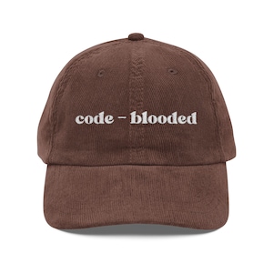 May include: A brown corduroy baseball cap with the white embroidered text "code-blooded". The cap features a curved peak and a rounded crown. A casual hat.