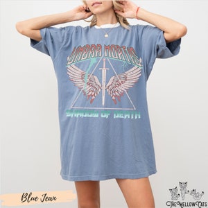 May include: A blue oversized t-shirt with a graphic print of a sword with wings and the text "UMBRA MORTIS SHADOW OF DEATH".