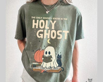Op de afbeelding: Mosgroen t-shirt met de tekst "THE ONLY GHOST I KNOW IS THE HOLY GHOST". Het shirt heeft een cartoon spook dat een boek leest, een pompoen en een zwarte kat. Het logo van The Mellow Cats staat rechtsonder.