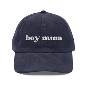 Könnte beinhalten: Eine marineblaue Baseballkappe aus Kord mit dem in weißem Garn aufgestickten Schriftzug "boy mum" auf der Vorderseite. Die Kappe verfügt über eine strukturierte Krone, einen gebogenen Schirm und einen Knopf an der Oberseite im klassischen Design.