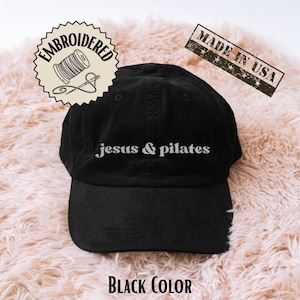 May include: Black corduroy baseball cap with the embroidered text "jesus & pilates" in white. The cap has a curved brim and a six-panel design. The image also includes a "Made in USA" stamp and a "Black Color" label.