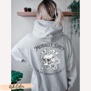 Op de afbeelding: Een grijs hoodie met de tekst "Morally Grey is my favorite color" en een zwart-witte illustratie van een schedel met bloemen en vlinders.