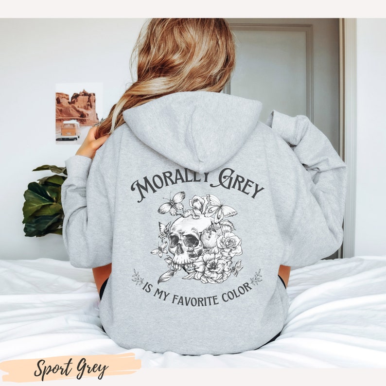 Op de afbeelding: Een grijs hoodie met de tekst "Morally Grey is my favorite color" en een zwart-witte illustratie van een schedel met bloemen en vlinders.