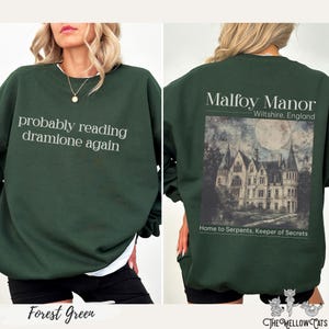 Könnte beinhalten: Grün-farbener Sweatshirt mit dem Text "probably reading dramione again" auf der Vorderseite und einem Grafikdruck von Malfoy Manor mit dem Text "Malfoy Manor, Wiltshire, England, Home to Serpents, Keeper of Secrets" auf der Rückseite.