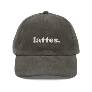 以下が含まれることがあります： 前面中央に白い小文字でlattes.と刺繍された、ダークグレーのコーデュロイ製ベースボールキャップ。この帽子は、6枚パネルの構造で、カーブしたつばとクラウン上部の中央にボタンが付いたデザインになっています。