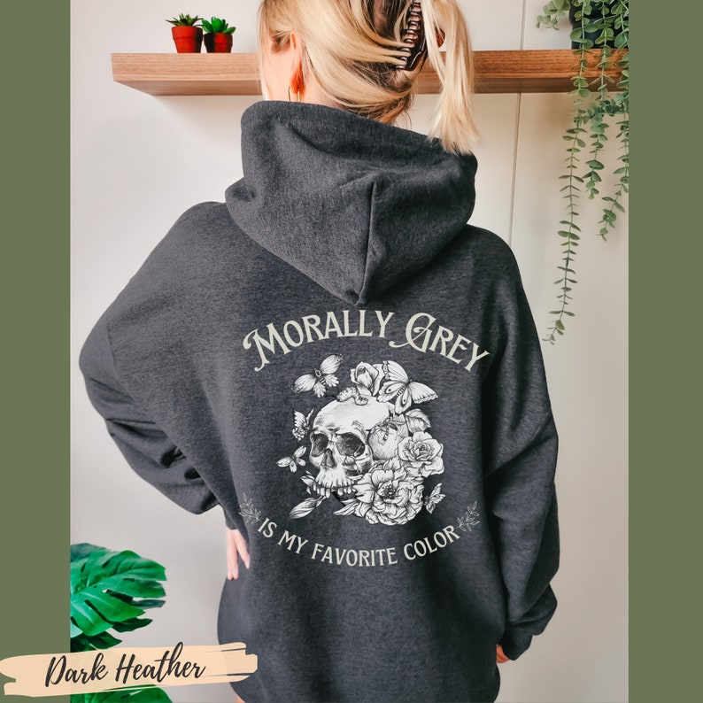 Op de afbeelding: Donkergrijze hoodie met een witte schedel en bloemenontwerp. De tekst "Morally Grey is my favorite color" staat op de achterkant.