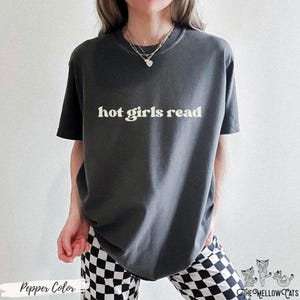 Puede incluir: Una camiseta gris oscura con el texto "hot girls read" impreso en blanco. La camiseta la lleva puesta una persona con un collar plateado.