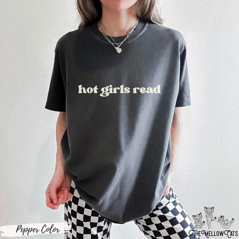 Puede incluir: Una camiseta gris oscura con el texto "hot girls read" impreso en blanco. La camiseta la lleva puesta una persona con un collar plateado.