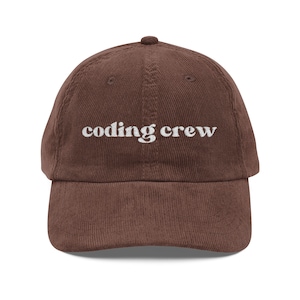 Può includere: Cappellino da baseball in velluto a coste marrone con la scritta "coding crew" ricamata in bianco. Il cappellino ha una visiera curva e un bottone sulla parte superiore. Un accessorio per chi lavora nel campo della programmazione.
