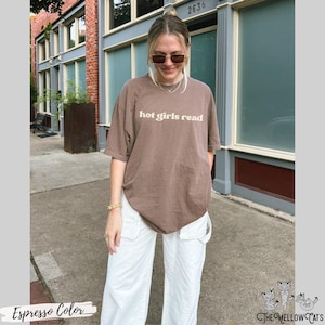 Puede incluir: Una camiseta marr&oacute;n con el texto "hot girls read" en blanco. La modelo lleva pantalones blancos y gafas de sol.