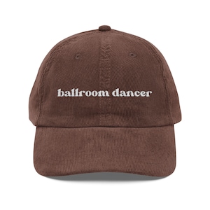 May include: A brown corduroy baseball cap with the embroidered text "ballroom dancer" in white. The cap has a curved brim and a rounded top.
