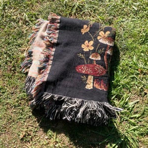 May include: Black woven throw blanket with a fringe border featuring a mushroom and flower design.