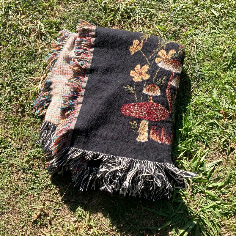 May include: Black woven throw blanket with a fringe border featuring a mushroom and flower design.
