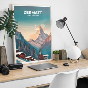 May include: A framed poster displaying the text "ZERMATT SWITZERLAND" showcases a mountain scene with red-roofed buildings. The poster is on a wooden desk with a laptop, lamp, and other accessories.