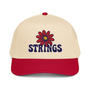 Könnte beinhalten: Cremefarbene Baseballkappe mit rotem Schirm und rotem Knopf. Die Kappe hat ein rot-gelbes Blumendesign über dem marineblauen, aufgestickten Wort "STRINGS" auf der Vorderseite.