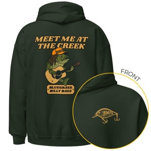 Puede incluir: Sudadera con capucha verde oscuro con un gráfico en la espalda que dice "Meet Me At The Creek" con un pez tocando la guitarra. La sudadera también tiene un pequeño gráfico de un señuelo de pesca en la parte delantera.