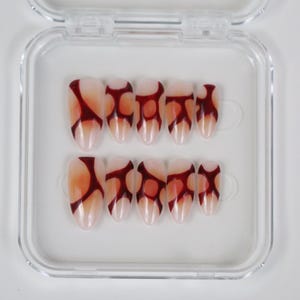 Peut inclure: Un ensemble de faux ongles ovales dans un &eacute;tui en plastique transparent. Les ongles sont rose p&acirc;le avec un motif abstrait rouge fonc&eacute;. Le motif est une s&eacute;rie de formes connect&eacute;es. L'&eacute;tui est transparent et rectangulaire.