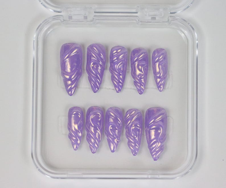 K&ouml;nnte beinhalten: Ein Set aus lavendelfarbenen Press-On-N&auml;geln mit Perlmutt-Finish. Die N&auml;gel befinden sich in einer transparenten Kunststoffbox und weisen ein geformtes Design auf. Das Set enth&auml;lt verschiedene Gr&ouml;&szlig;en f&uuml;r eine individuelle Passform.