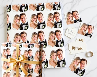 May include: Wedding-themed gift wrap and tags featuring a repeating pattern of a smiling couple in formal attire. A wrapped gift box with a gold bow sits next to loose tags and a wedding ring.