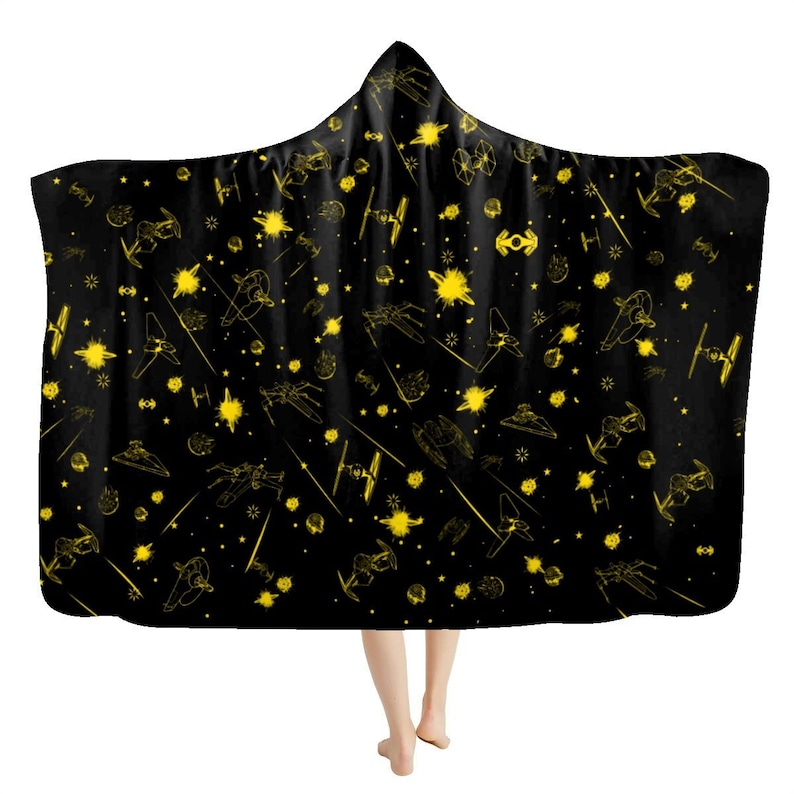 K&ouml;nnte beinhalten: Schwarze Kapuzen-Decke mit goldenem Weltraumschlacht-Design. Die Decke zeigt verschiedene Raumschiffe, Explosionen und Sternenmuster. Diese Kapuzen-Decke ist ein gem&uuml;tliches Accessoire f&uuml;r Fans von Weltraumfilmen und -shows.